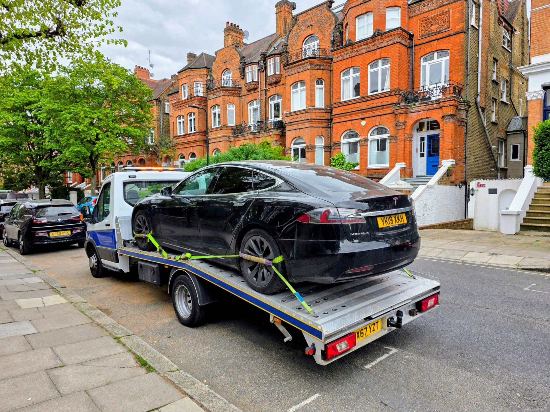 Black Tesla Model S on a flatbed tow truck for electric car recovery Kensington. Expert EV towing service in W8.