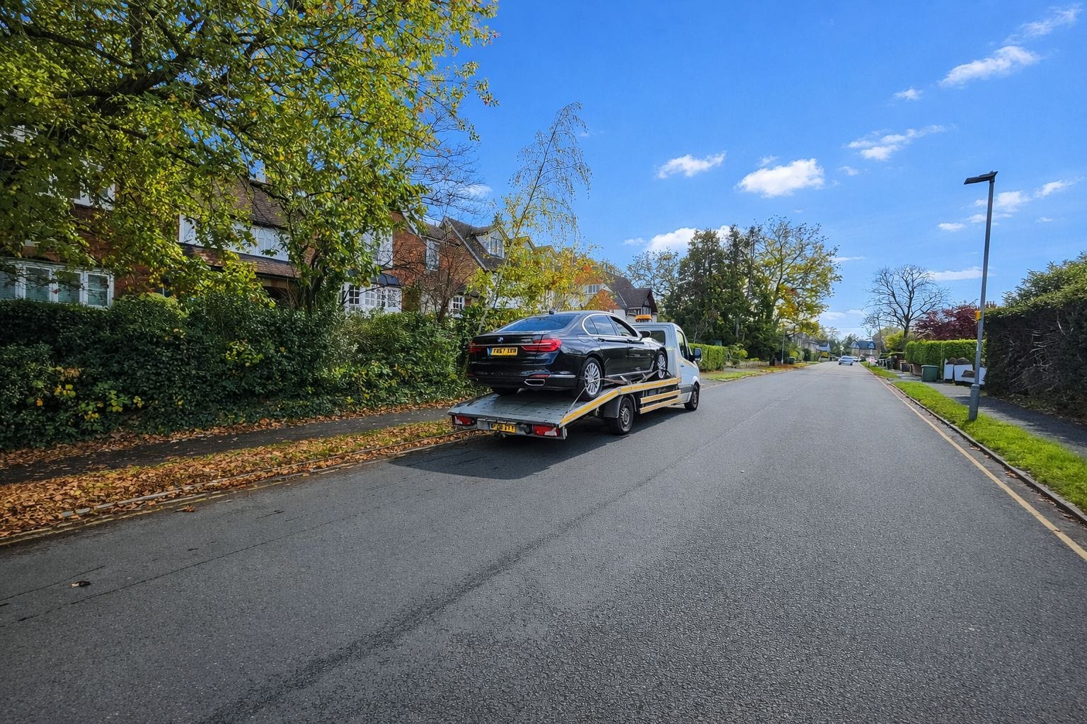 London Auto Towing flatbed truck recovering a black luxury saloon car on a leafy residential road in Kensington.